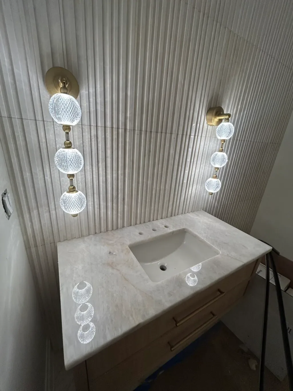Powder room with floating wood vanity, stone top, fluted paneling, and glass sconces