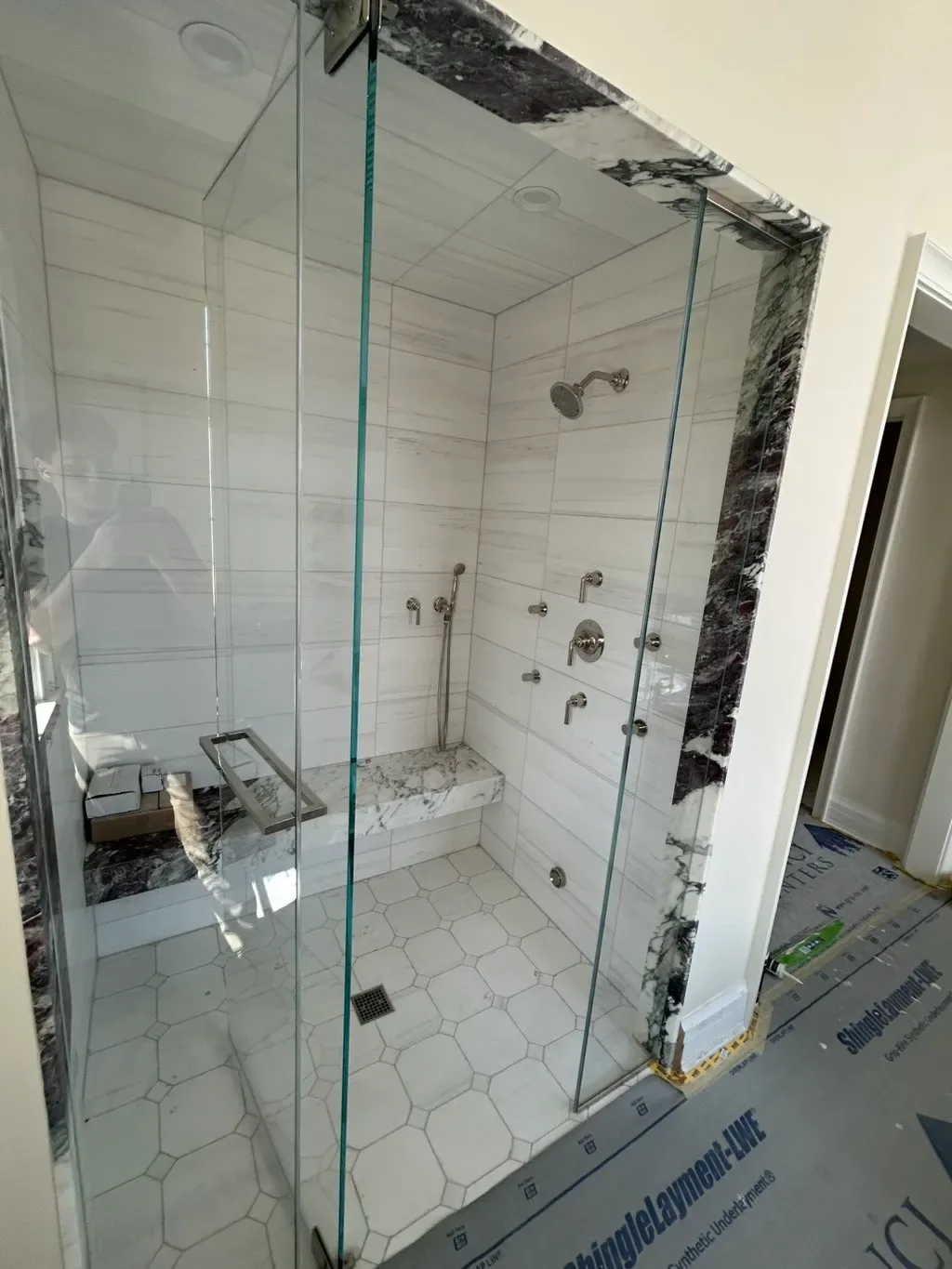 Frameless glass shower enclosure being fitted, protective film still on